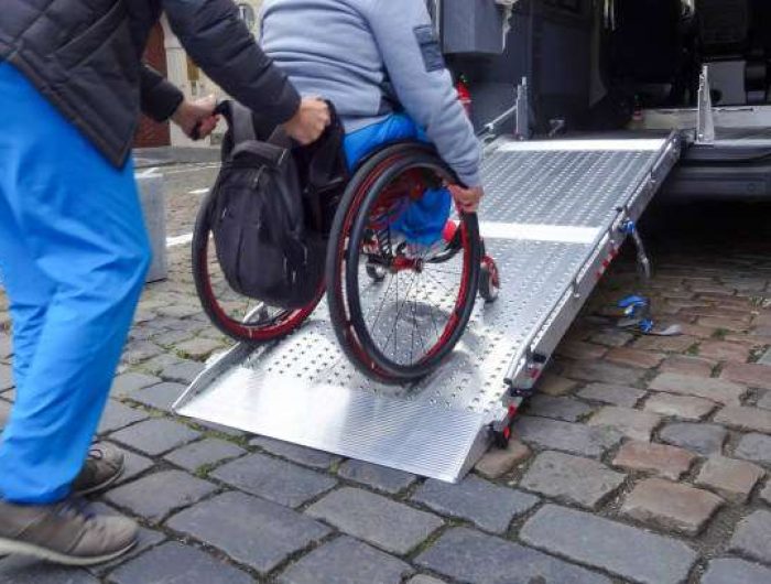 Assistant helping disabled person on wheelchair with transport using accessible van ramp